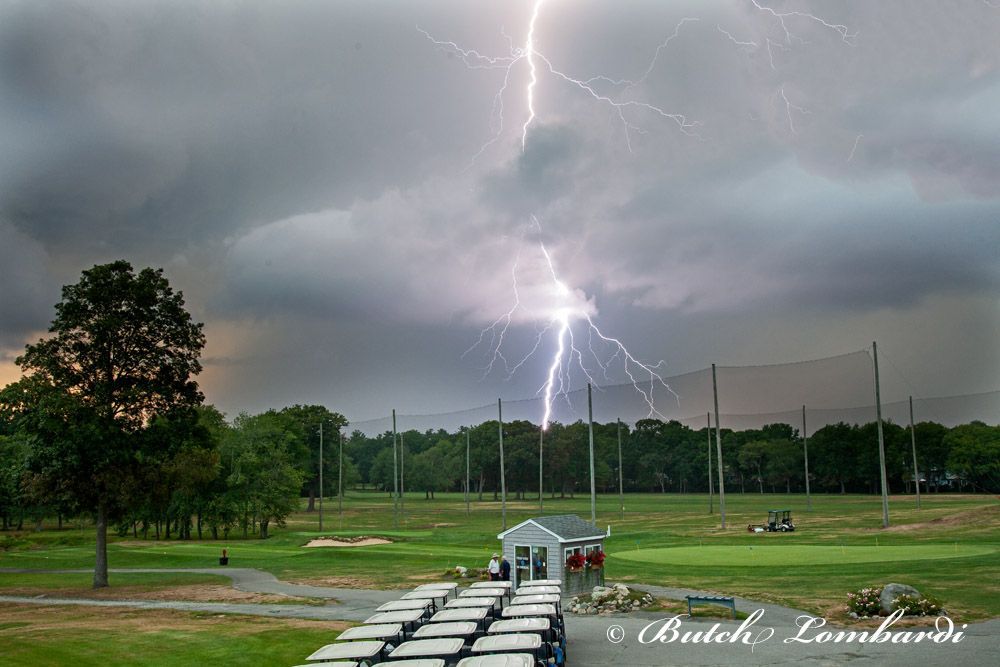 A lightning bolt is striking a golf course with a row of golf carts in the foreground.