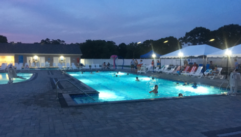 A large swimming pool is lit up at night with people swimming in it.