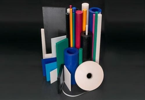 Variadas varillas, tubos y láminas de plástico de colores dispuestos sobre una superficie oscura.