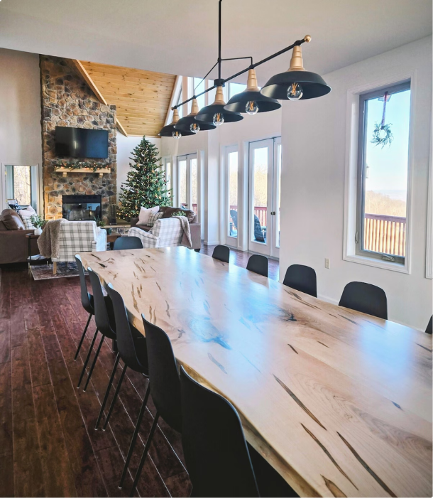 Dining room with light-wood table, black chairs, chandelier, and fireplace view.