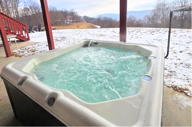 Steaming hot tub on snowy patio with winter landscape.