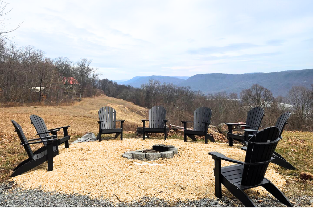 Seven black Adirondack chairs around fire pit with valley view.