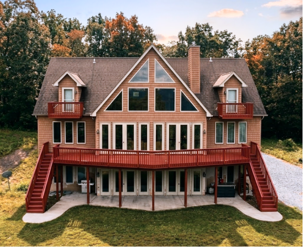 Large wooden house with deck, red railings, and autumn trees.