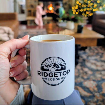 Hand holding white mug with Ridgetop Lodge logo.