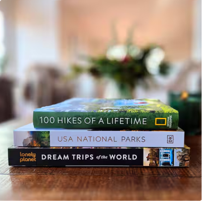 A stack of three travel books on a wooden table with a blurred background.