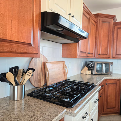 Kitchen counter with gas stove, range hood, and utensils.