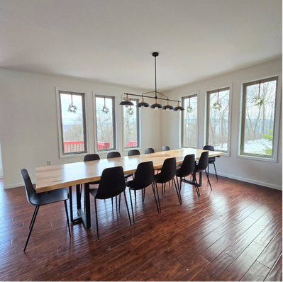Wooden dining table with black chairs in sunlit room.