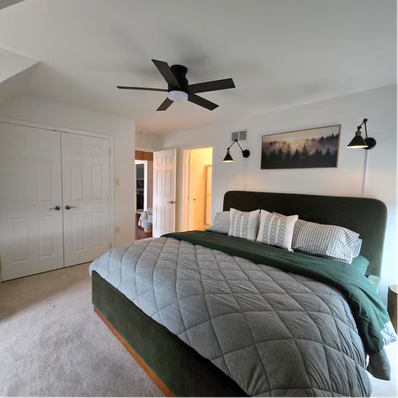 Cozy bedroom with green bed, quilted bedding, and wall lamps.