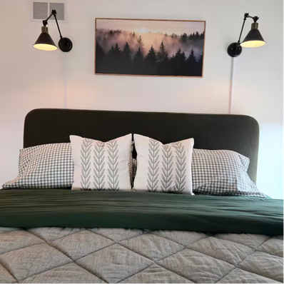 Bed with green headboard, patterned pillows, and wall lamps.