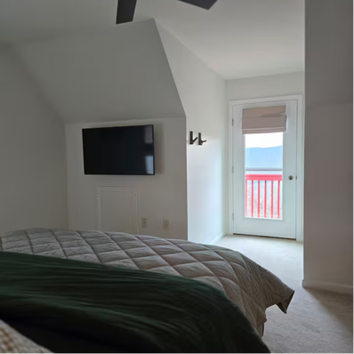 Bedroom with quilted bed, wall-mounted TV, and balcony view.
