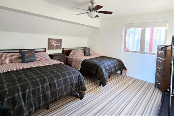 Bedroom with two queen beds, plaid comforters, and wood dresser.