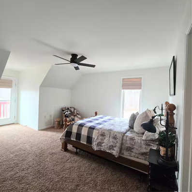 Bedroom with queen bed, buffalo check comforter, and ceiling fan.