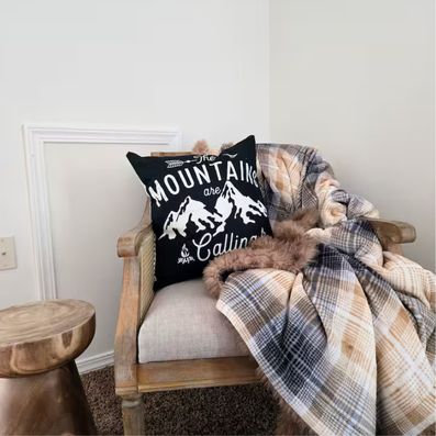 Wooden chair with “The Mountains Are Calling” pillow and plaid blanket.