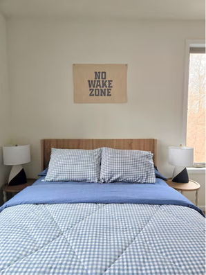Bed with blue checkered bedding, bedside lamps, and wall sign.