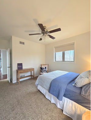 Bright bedroom with blue bed, wooden console, and ceiling fan.