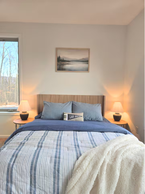 Bed with blue-striped bedding, wood headboard, and lamps.
