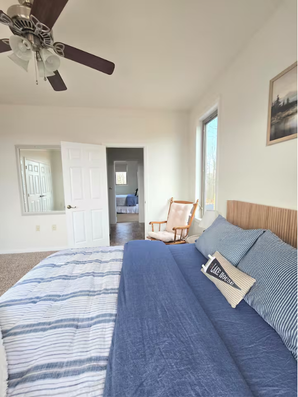 Bedroom with blue-striped bed, ceiling fan, and rocking chair.