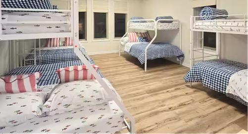 Dormitory room with three white bunk beds and patterned bedding.