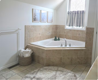 Corner bathtub with beige tile, towels, and small window.
