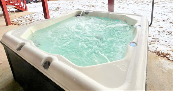 Steaming hot tub on snowy concrete patio.