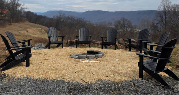 Six black Adirondack chairs around stone fire pit with mountain view.