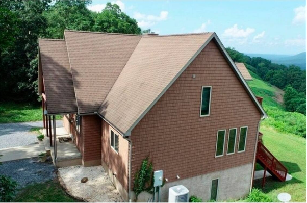 Aerial view of brown-shingled house on grassy hillside.