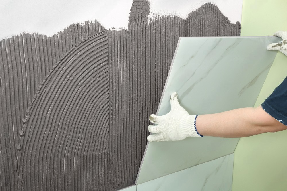 a person is holding a tile while applying adhesive to a wall .