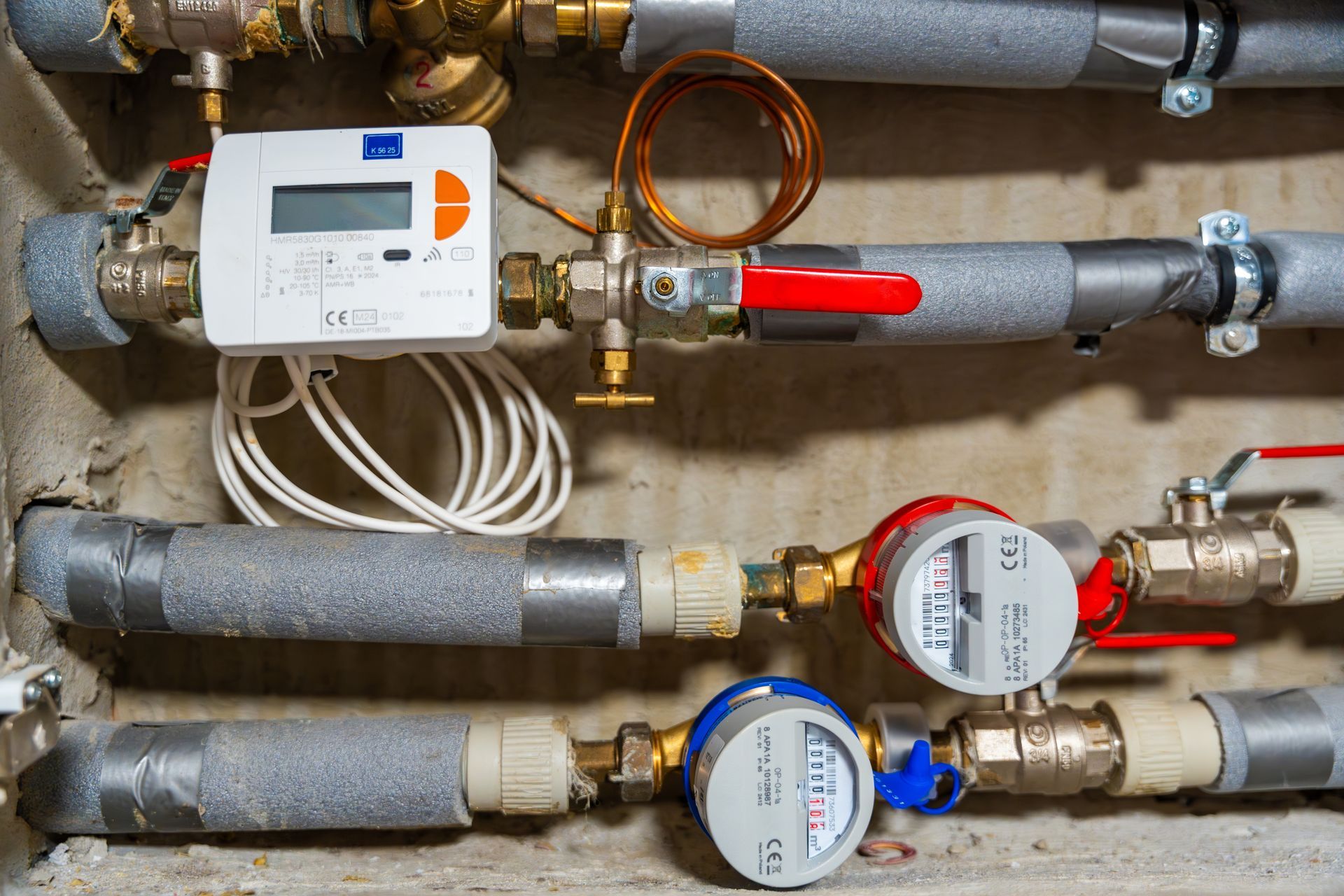 A close up of a water meter surrounded by pipes and valves.