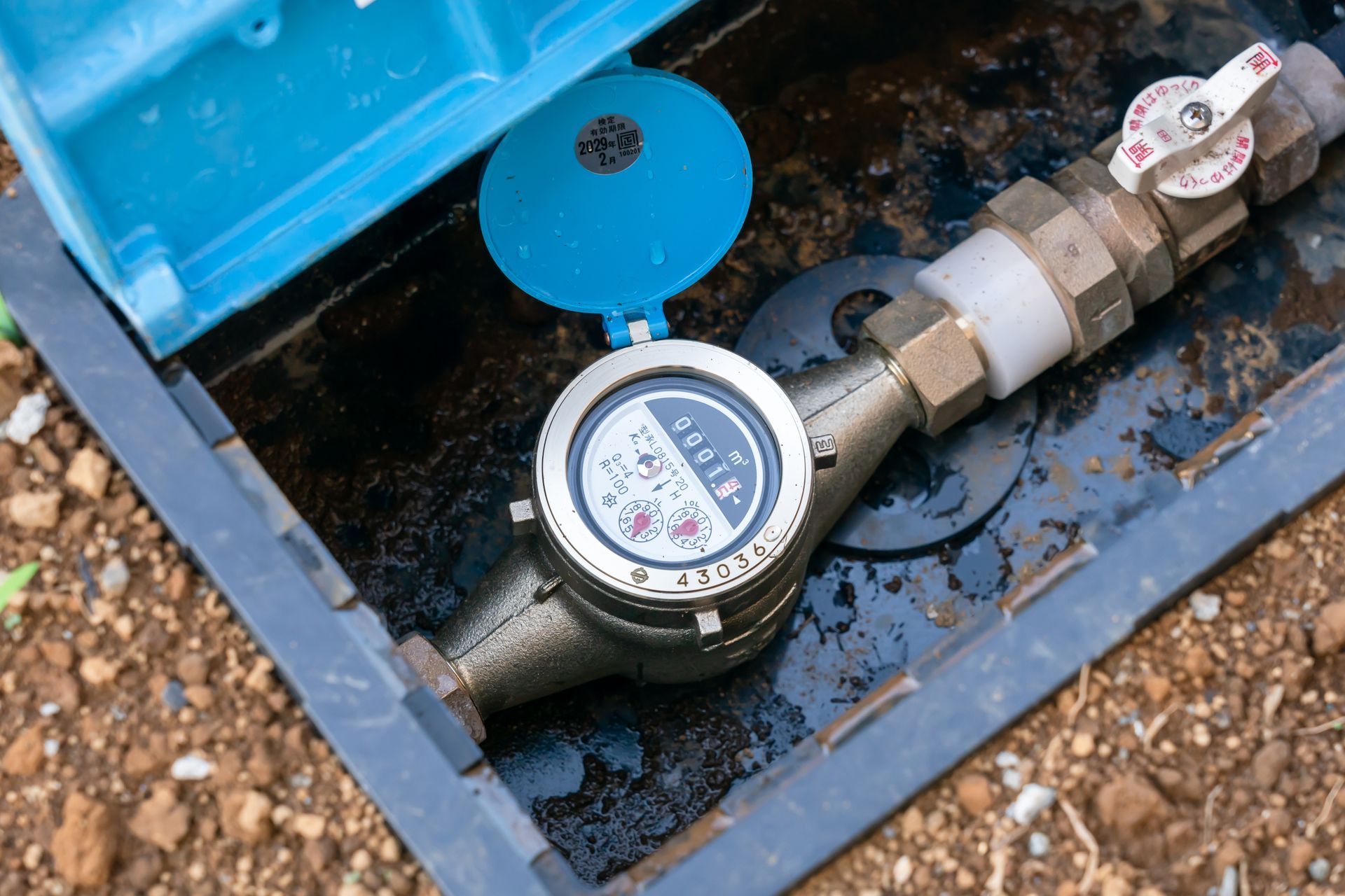 A water meter is sitting in a box on the ground.