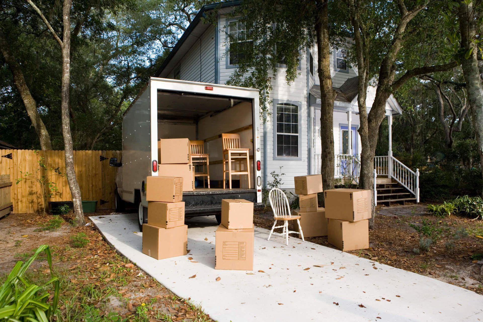 Moving truck parked in driveway, loaded with boxes and furniture in front of a house.
