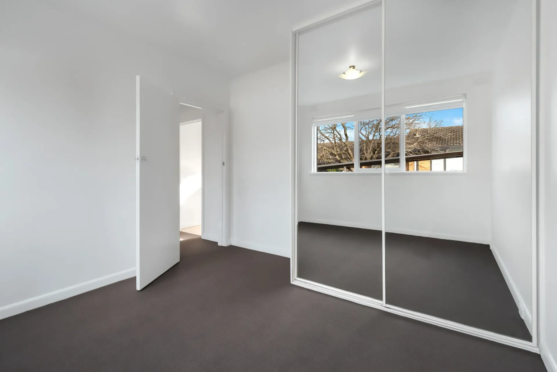 An empty bedroom with a large mirrored wardrobe.