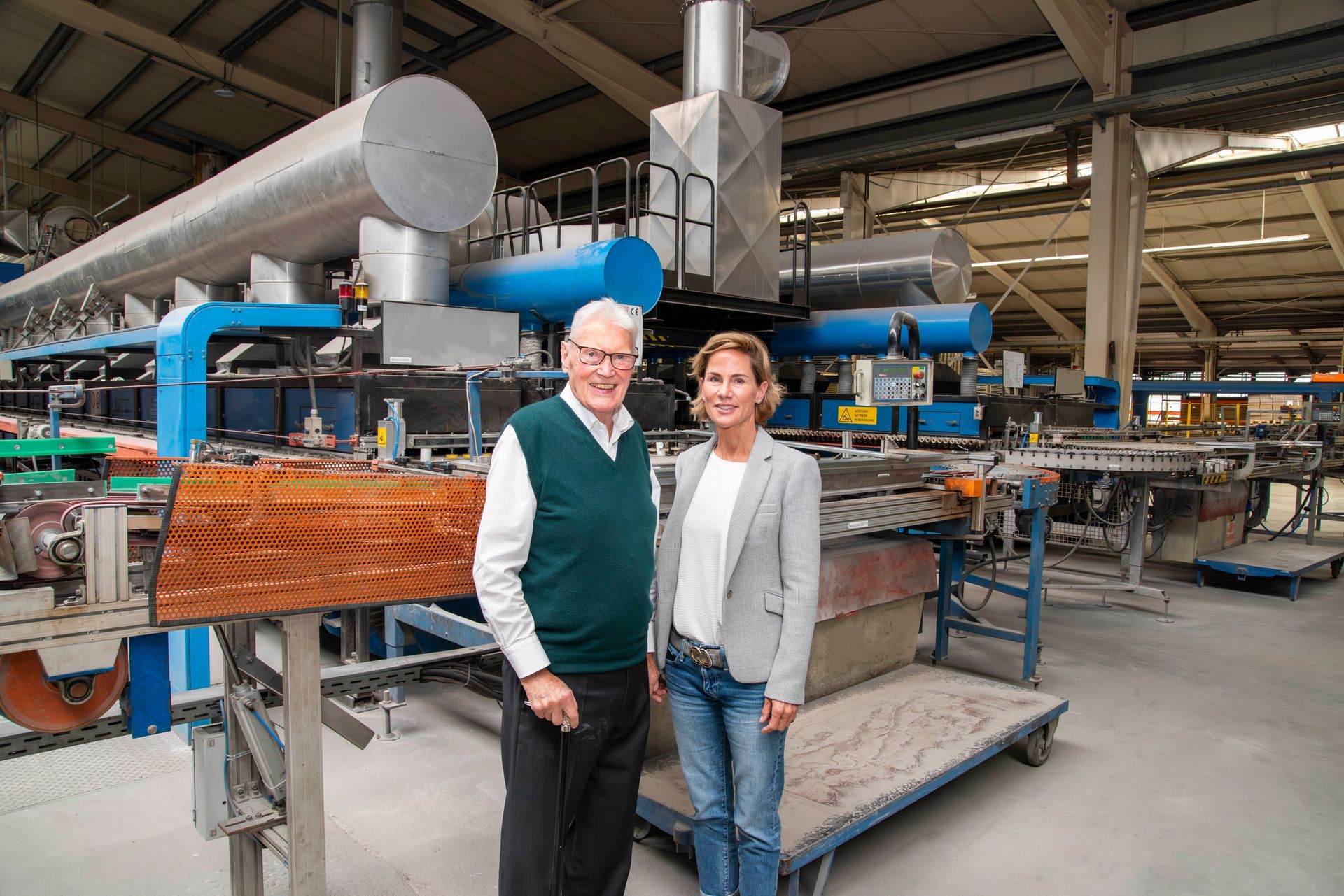 A man and a woman are standing in front of a machine in a factory.