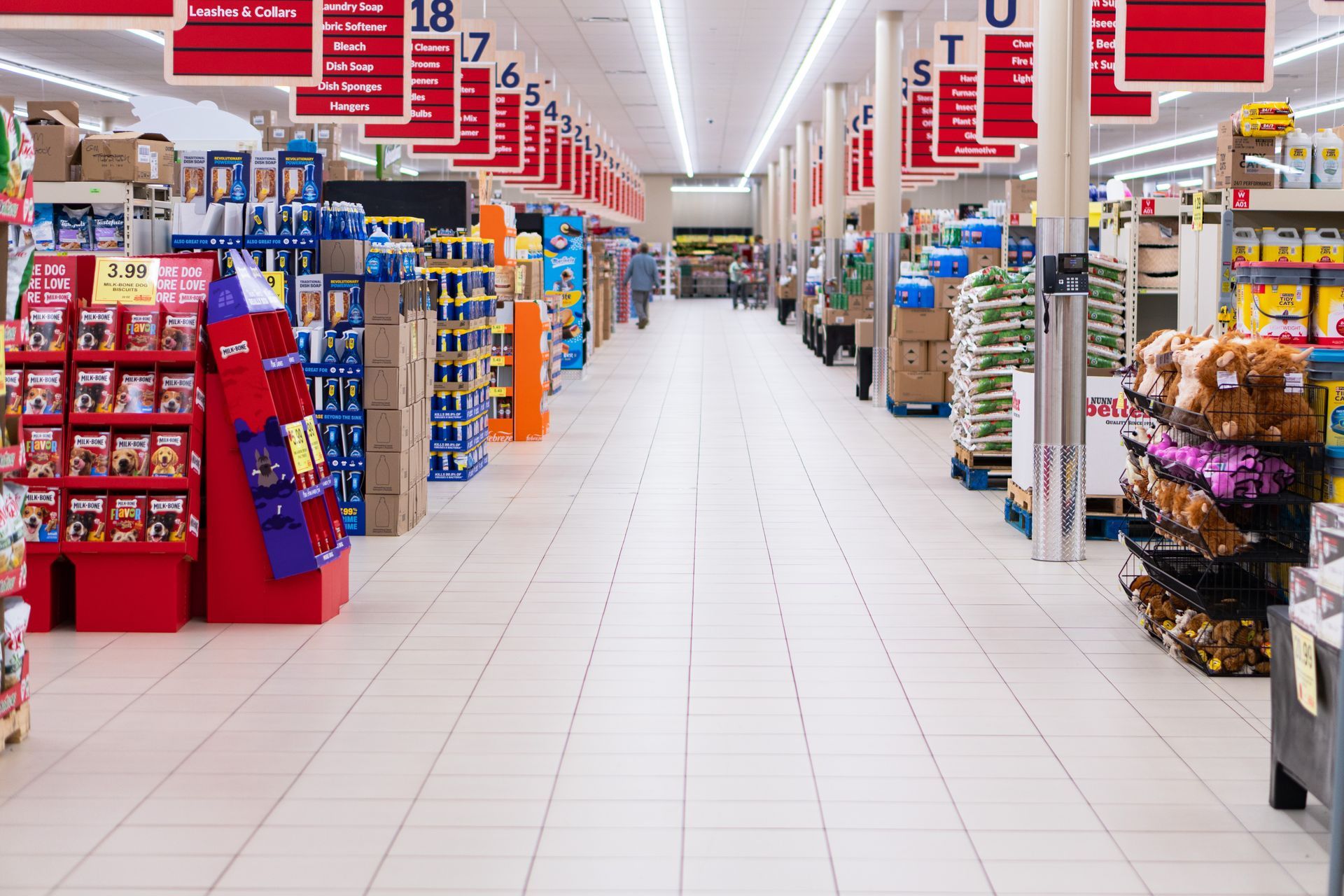 Grocery store aisle with products on shelves, overhead signs, and tiled floor.