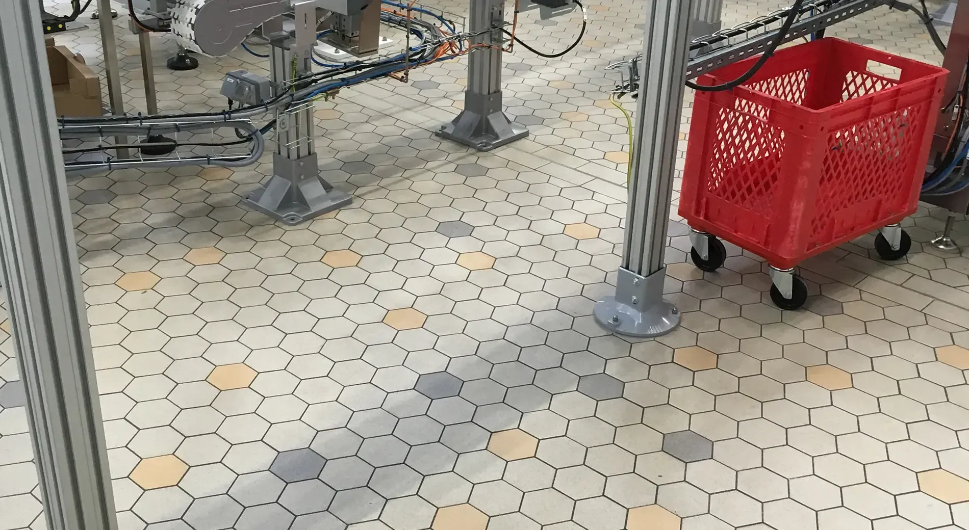 A red basket is sitting on a tiled floor in a factory.