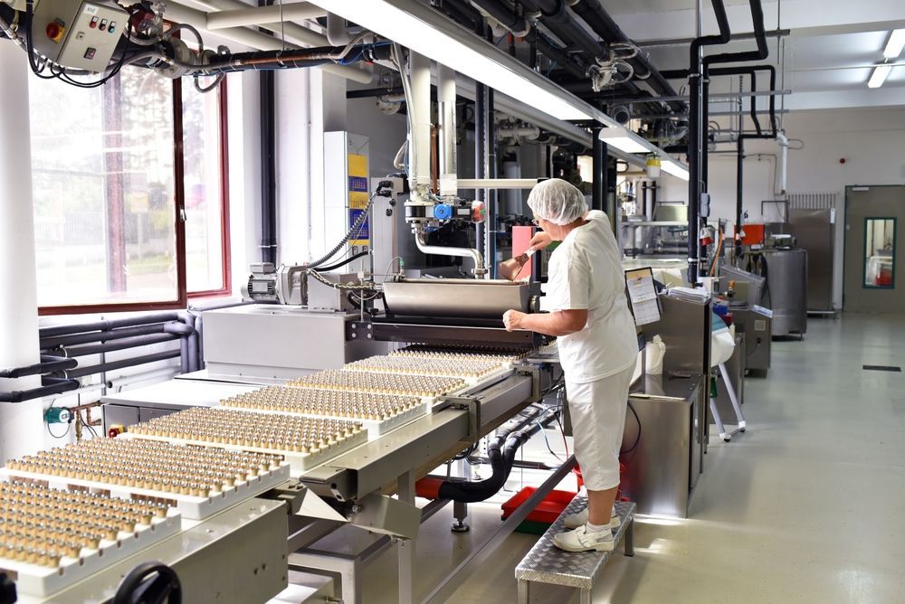 A person in white sanitary clothing operates a filling machine for small bottles on an industrial production line.
