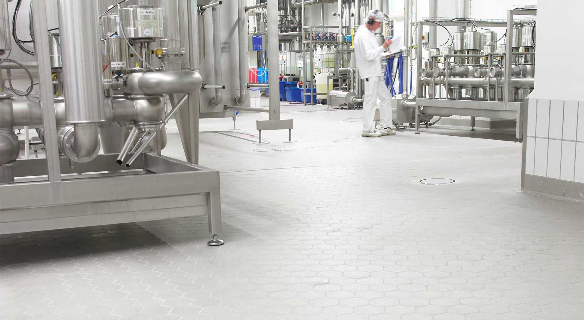 A person in protective white clothing works in a sterile, industrial food processing facility filled with steel machinery.