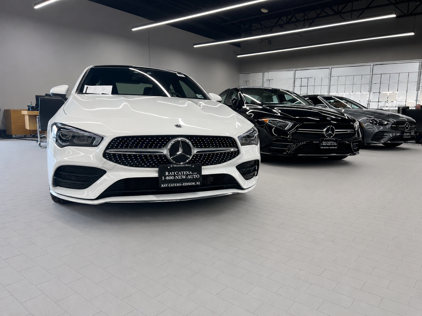 White Mercedes-Benz sedan in a showroom, with black cars lined up behind it.