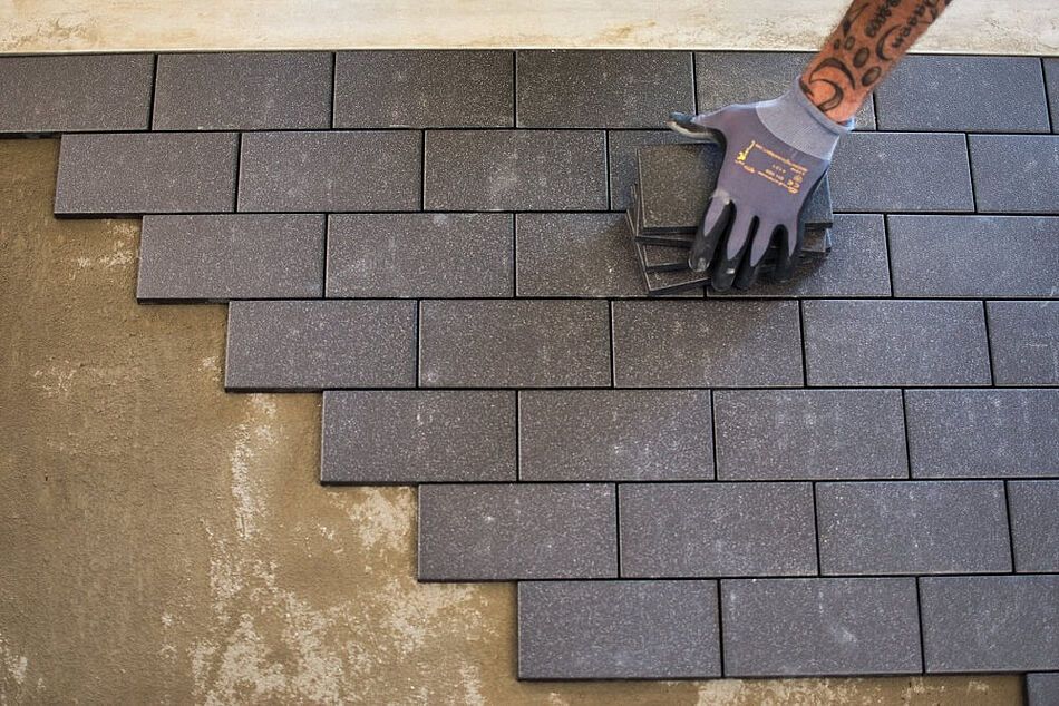 A person wearing gloves is laying bricks on the floor.