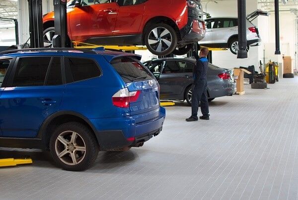 A man is standing next to a blue car in a garage.