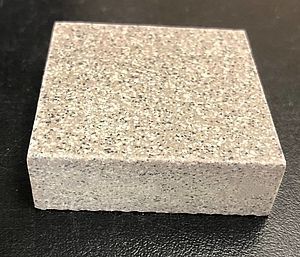 A small square piece of granite is sitting on a black surface.