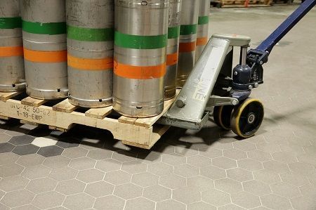 A hand truck is pushing a pallet of kegs in a warehouse.