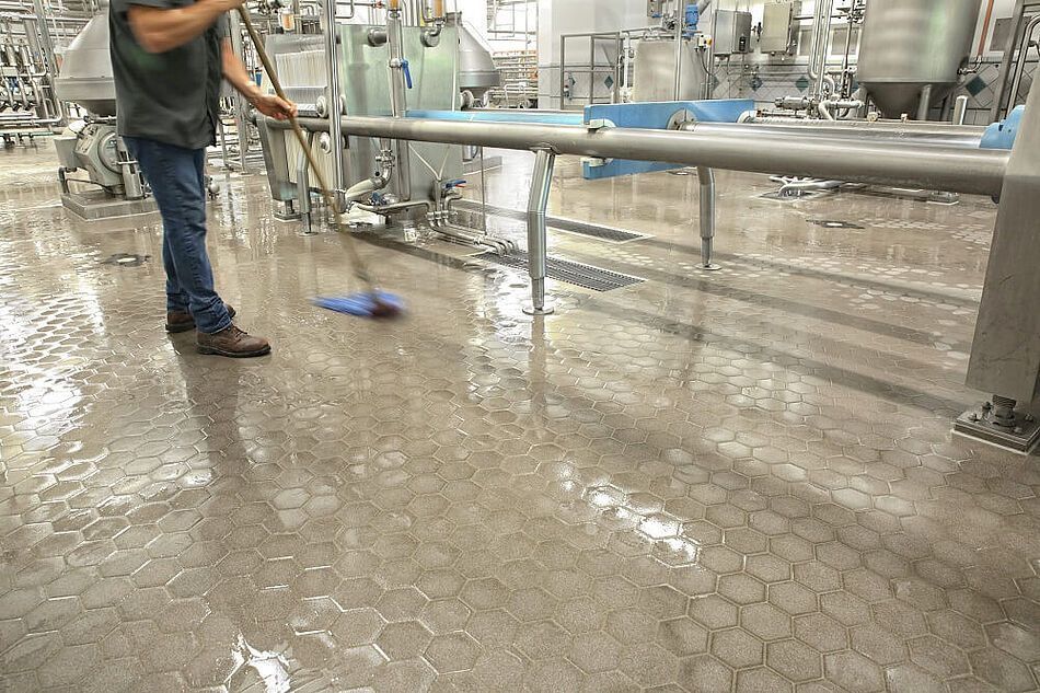 A man is cleaning the floor of a factory with a mop.