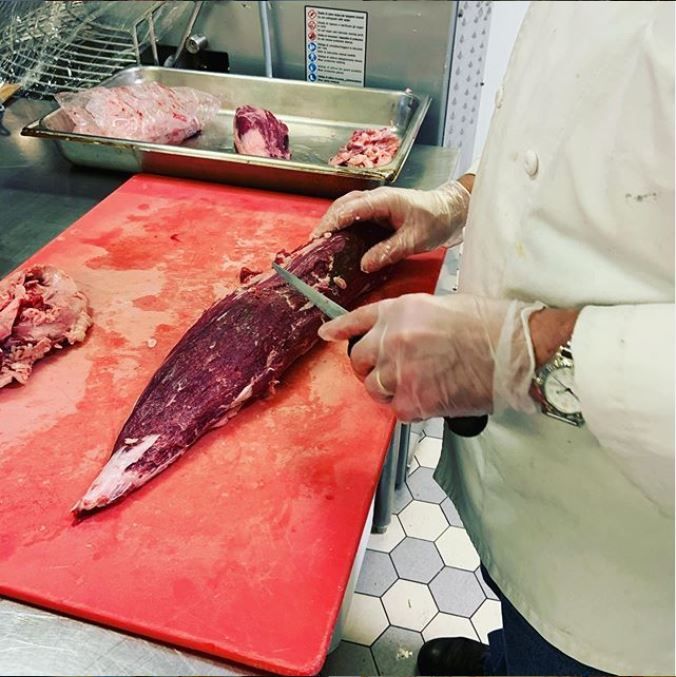 A person is cutting a large piece of meat on a red cutting board