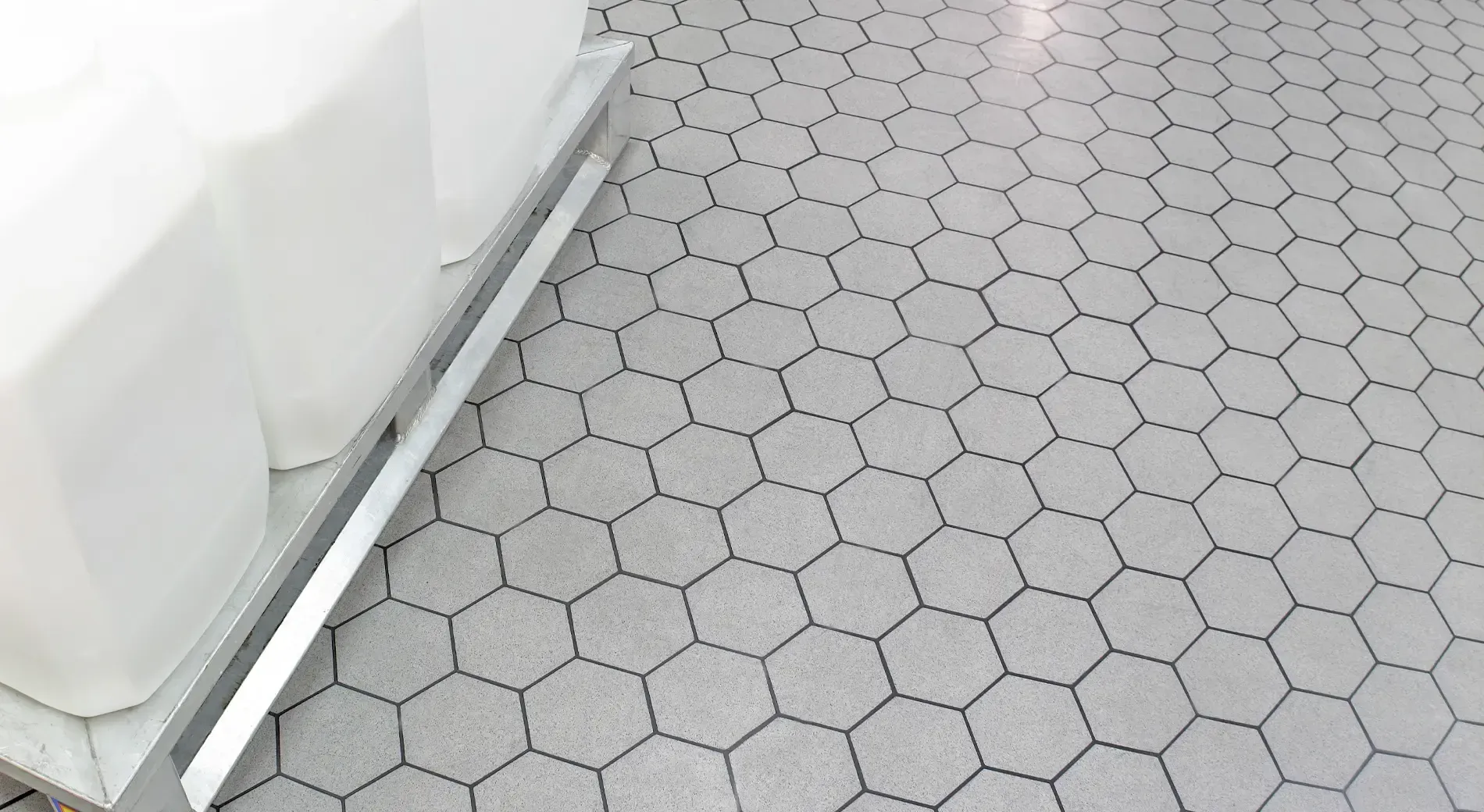 A close-up view of light gray hexagonal floor tiles next to the white base of a display shelf.