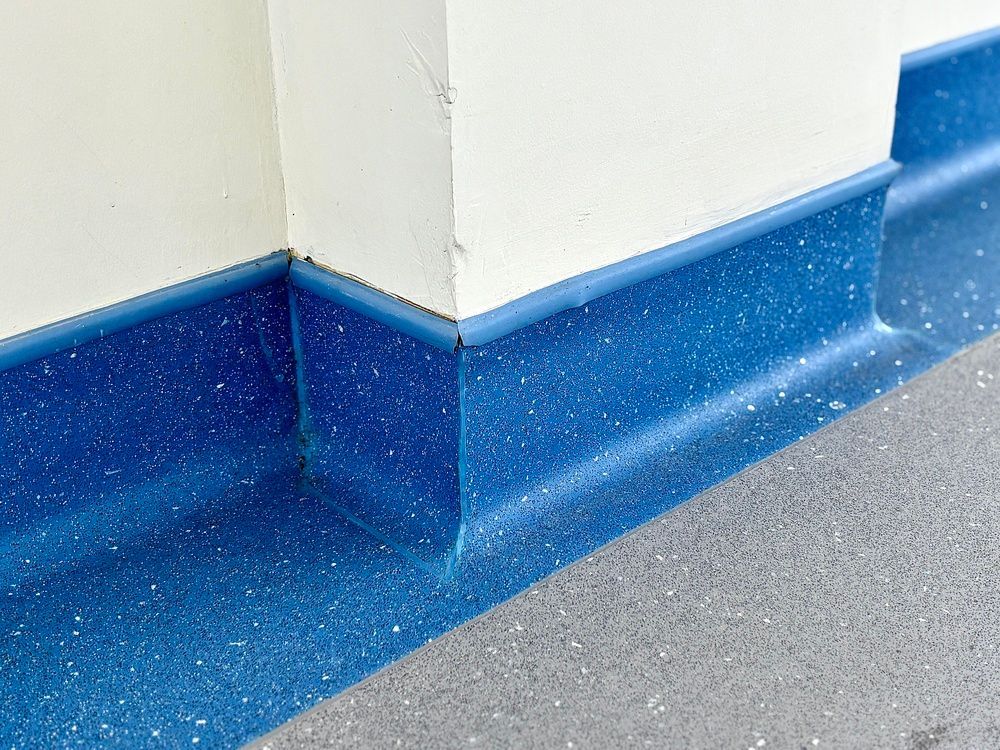 Blue vinyl coved skirting board installed against a white wall and grey flooring.