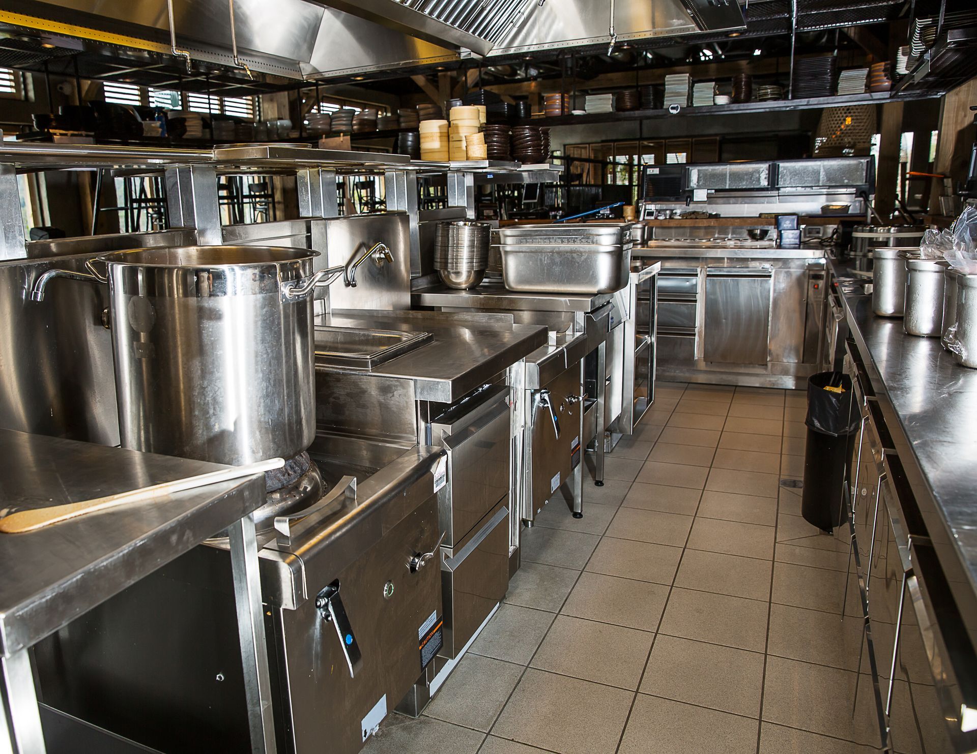 A kitchen with lots of stainless steel appliances and pots and pans, and a quarry tile floor