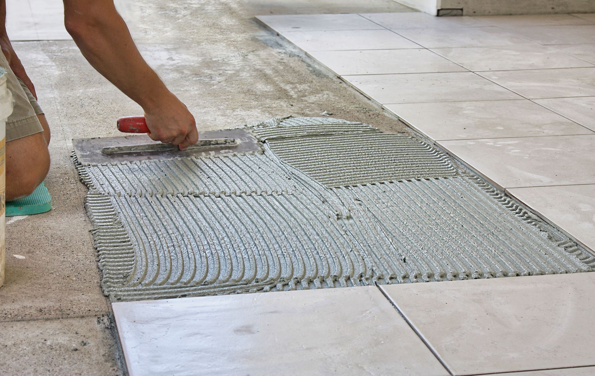 A person is laying tiles on concrete subfloor with a trowel