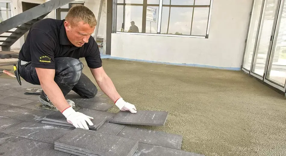 A man is kneeling down on a tiled floor in a room.