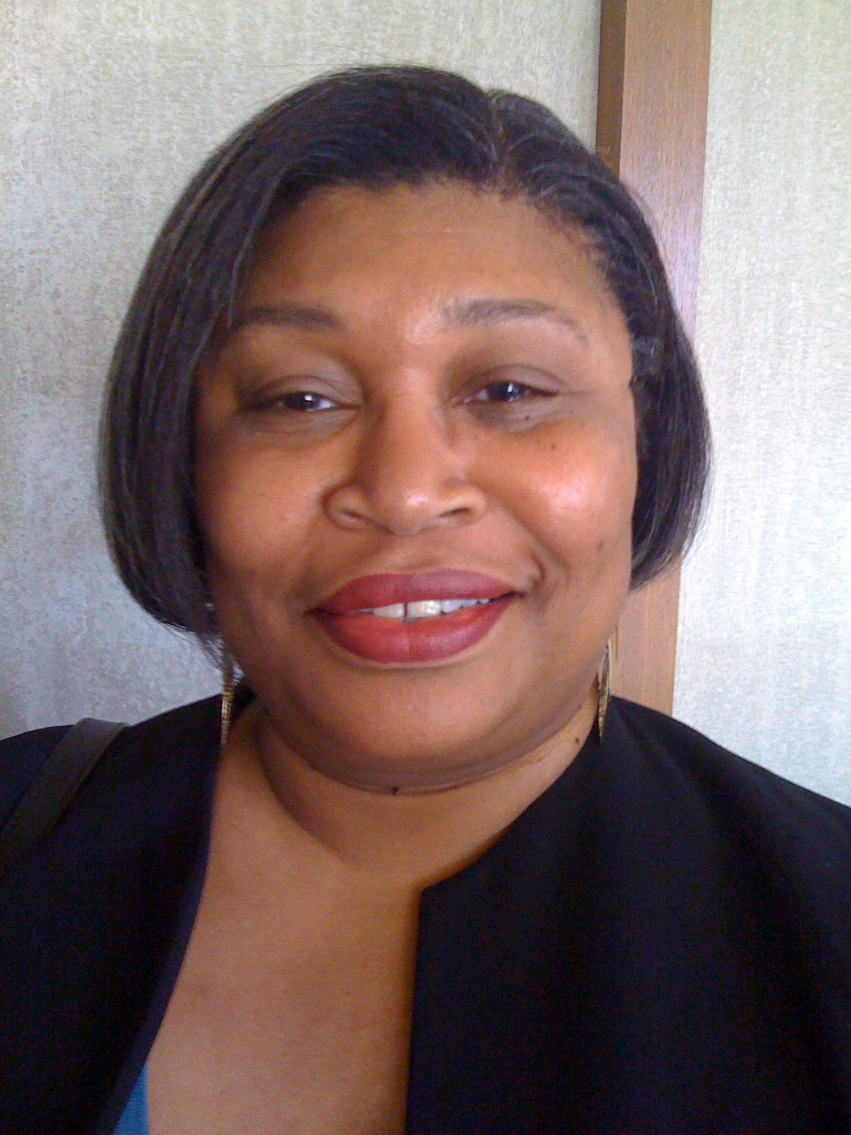 A woman wearing a black jacket and red lipstick is smiling for the camera.