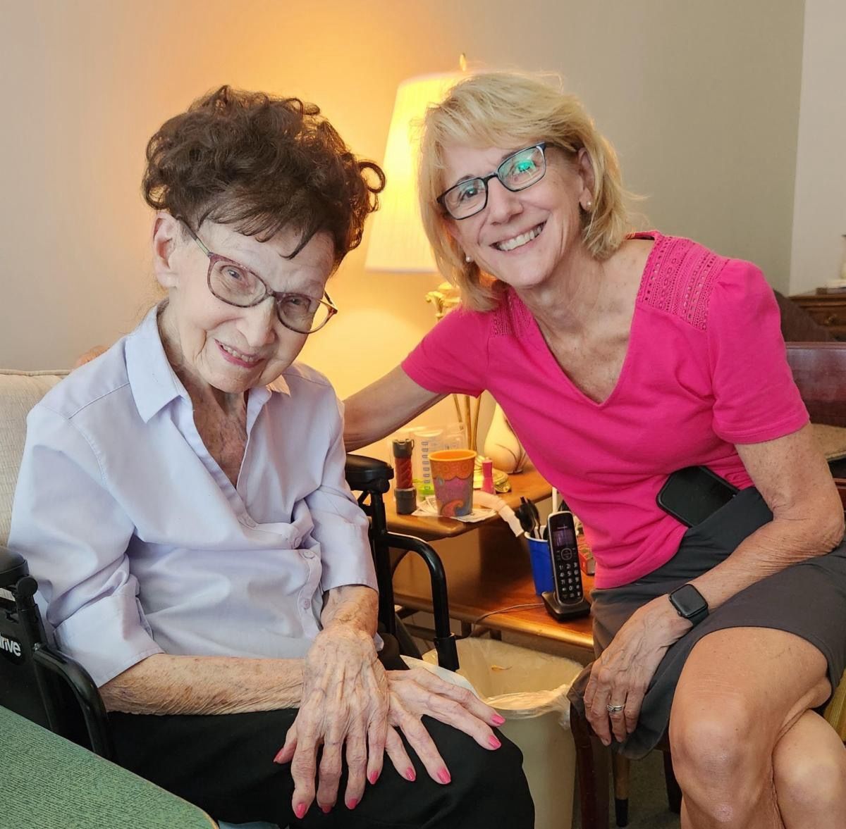 A woman is sitting next to an older woman in a wheelchair.